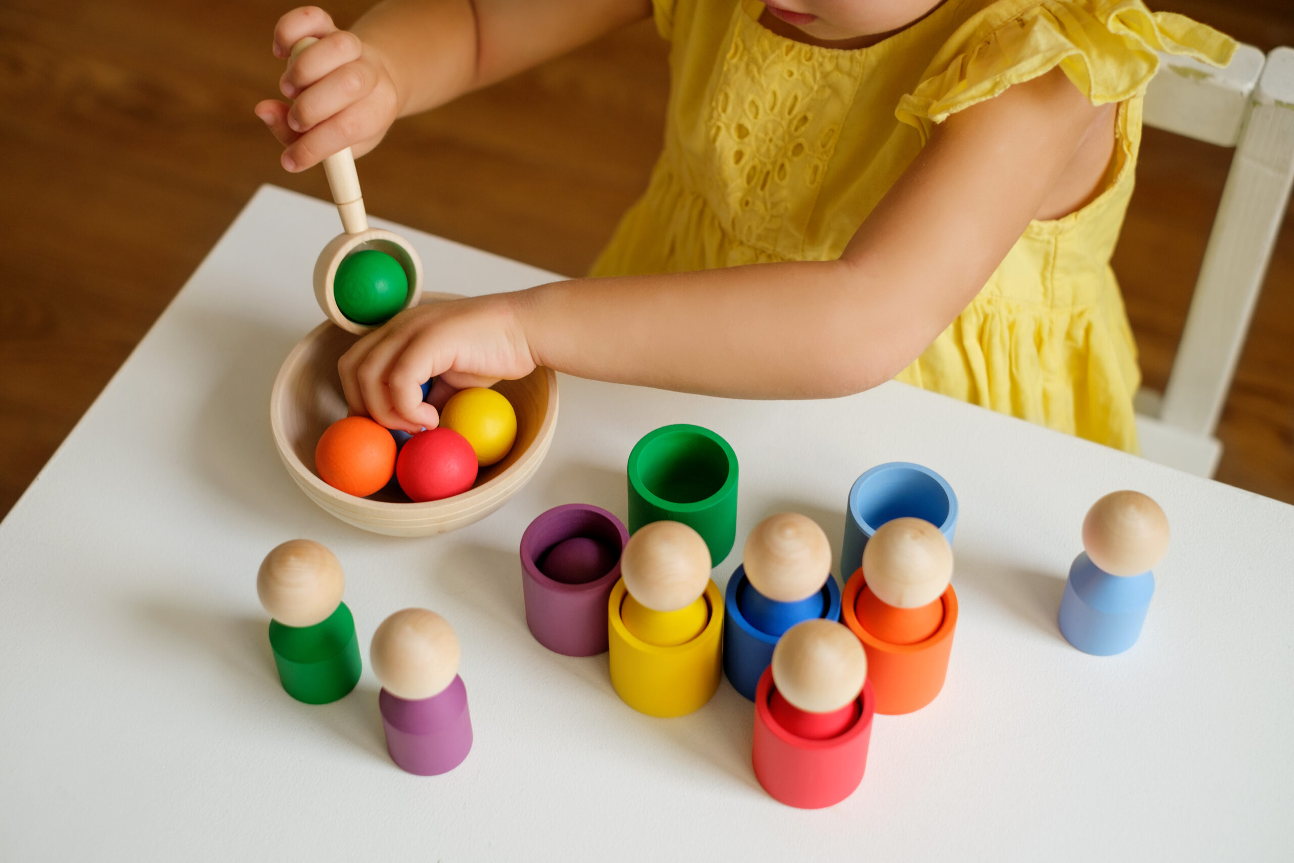 A sorter toy for preschool development: balls in cups. Wooden multi-colored figures, balls, cylinders with a spoon and a plate for sorting by color. Development of fine motor skills of the hands